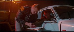 A tow truck driver gets a dying accident victim to sign a waiver in Brian Trenchard-Smith's Dead-End Drive-In (1986)