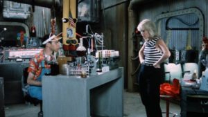 Evil nerd Menlo Schwartzer (Eddie Deezen) explains his plans to sidekick Sparkle (Linda Kerridge) in Randall Badat's Surf II (1983)