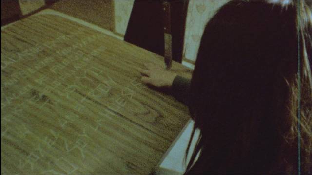In a trance, Altair (Diana Bovio) carves words into the kitchen table in Victor Dryere’s 1974: La posesión de Altair (2016)