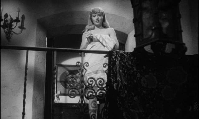 Phyllis Dietrichson (Barbara Stanwyck) stands wrapped in a towel at the top of the stairs in Billy Wilder’s Double Indemnity (1944)